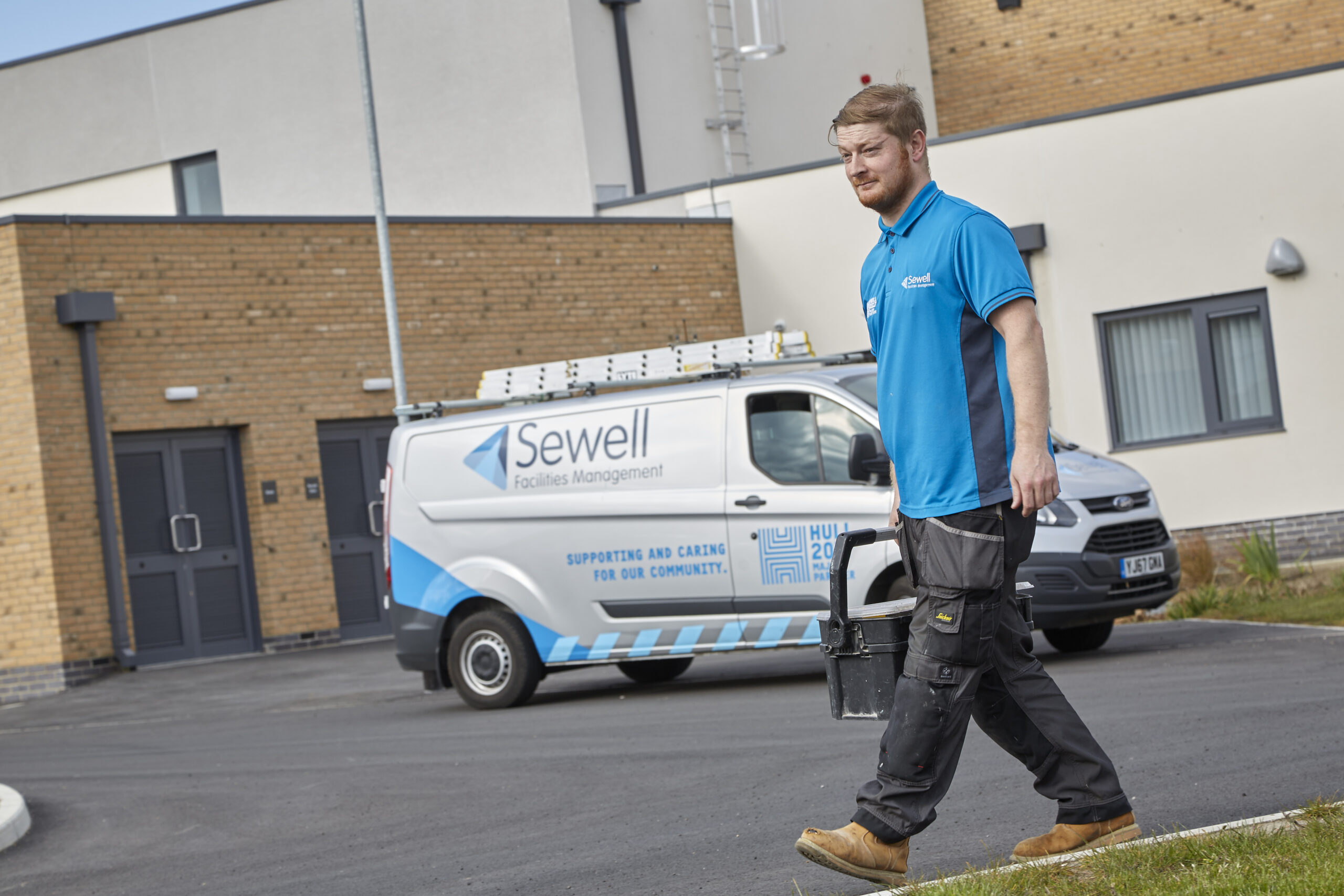 A Sewell FM technician with a toolbox walks from a van into a building